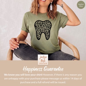 May include: A green t-shirt with a black and brown leopard print tooth graphic. The text "Jaclyn Rose DESIGN" is printed on the bottom of the shirt. The shirt is being modeled by a person. The text "Happiness Guarantee" is printed below the image. The text "We know you will love your shirt! However, if there is any reason you are unhappy with your purchase please message us within 14 days of purchase and a full refund will be issued." is printed below the text "Happiness Guarantee".