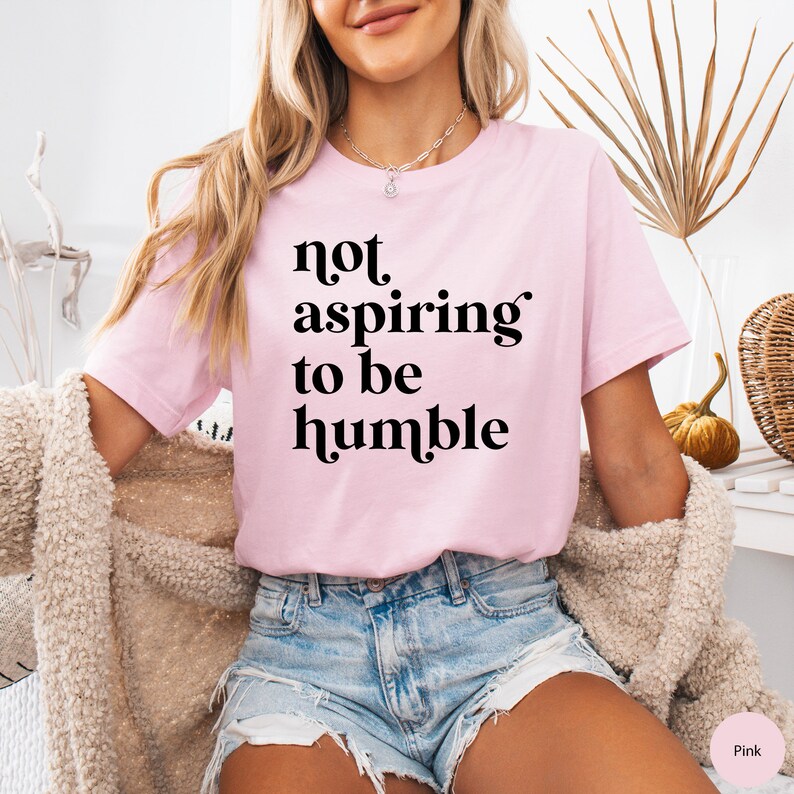 May include: A pink t-shirt with the text "not aspiring to be humble" printed in black.