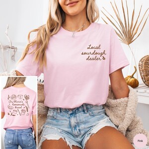 Pu&ograve; includere: T-shirt rosa chiaro con la scritta "Local sourdough dealer" sul davanti. Il retro della maglietta presenta la scritta "Olivia's homemade bread" con illustrazioni di panetteria. La maglietta &egrave; abbinata a pantaloncini di jeans.