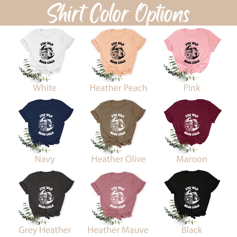Puede incluir: Una maqueta de una camiseta con el texto "Stay Wild Moon Child" en fuente blanca sobre un gr&aacute;fico de luna y estrellas negras. La camiseta se muestra en 10 colores diferentes: blanco, melocot&oacute;n jaspeado, rosa, azul marino, oliva jaspeado, granate, gris jaspeado, malva jaspeado y negro.