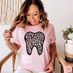 May include: A pink t-shirt with a black leopard print tooth graphic. The shirt is made of a soft, comfortable material.