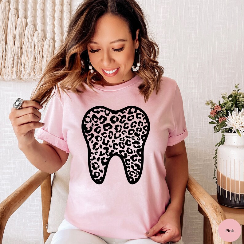 May include: A pink t-shirt with a black leopard print tooth graphic. The shirt is made of a soft, comfortable material.