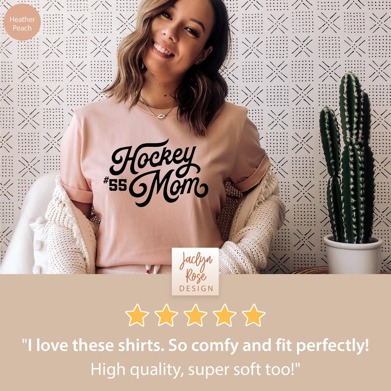 Peut inclure: Un t-shirt rose avec un texte noir qui dit "Hockey #55 Mom". Le t-shirt est port&eacute; par une personne et est photographi&eacute; sur un fond blanc avec un motif noir et blanc. L'image comprend &eacute;galement un cactus dans un pot.