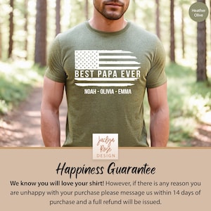 May include: A green t-shirt with a distressed American flag design and the text "Best Papa Ever" with the names "Noah - Olivia - Emma" underneath. The shirt is being worn by a person in a forest setting.