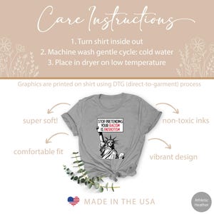Peut inclure: T-shirt gris avec un graphique de la Statue de la Libert&eacute; tenant une pancarte qui dit "Stop Pretending Your Racism Is Patriotism". Le t-shirt est fabriqu&eacute; aux &Eacute;tats-Unis et est super doux, confortable et a un design vibrant.