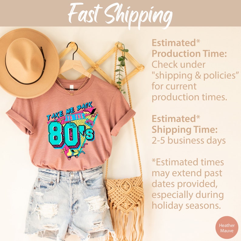 Pu&ograve; includere: Una t-shirt color malva con una stampa grafica retr&ograve; degli anni '80 che dice "Take Me Back to the 80s". La t-shirt &egrave; appesa a un appendiabiti di legno con un cappello di paglia e una borsa intrecciata.