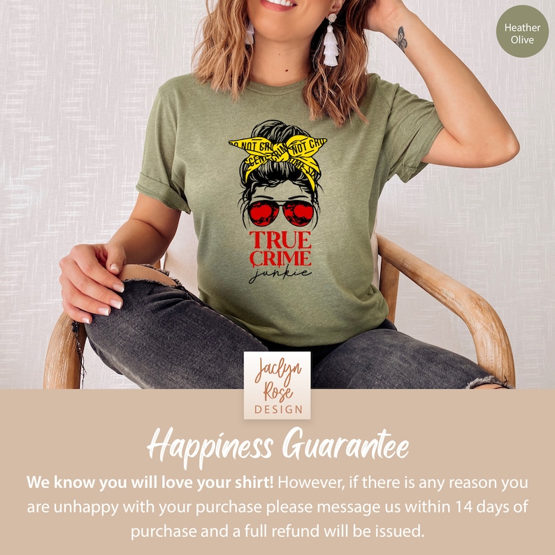 May include: A green t-shirt with a graphic of a woman with a messy bun and sunglasses. The text "TRUE CRIME junkie" is printed on the shirt. The shirt is available in Heather Olive.