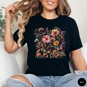 K&ouml;nnte beinhalten: Schwarzes T-Shirt mit einem Blumendruck mit verschiedenen rosa, orangefarbenen und gelben Blumen.