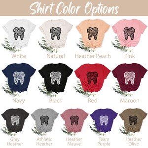 May include: A selection of t-shirts in various colors, featuring a white tooth with a leopard print design. The colors include white, natural, heather peach, pink, navy, black, red, maroon, grey heather, athletic heather, heather mauve, team purple, and heather olive.