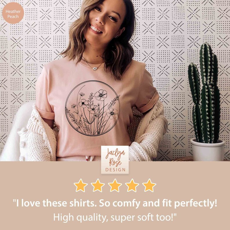 May include: A pink t-shirt with a black and white floral design in a circle. The shirt has a crew neck and short sleeves. The text "Jaclyn Rose DESIGN" is printed on the bottom of the shirt. The shirt is on a model and has a five-star rating.