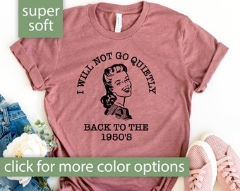 Puede incluir: Una camiseta de color malva con un gráfico retro de una mujer con el texto "No volveré a los años 50 en silencio".