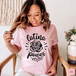 May include: A pink t-shirt with the text "latina power" in black lettering. A black rose graphic is centered above the text.
