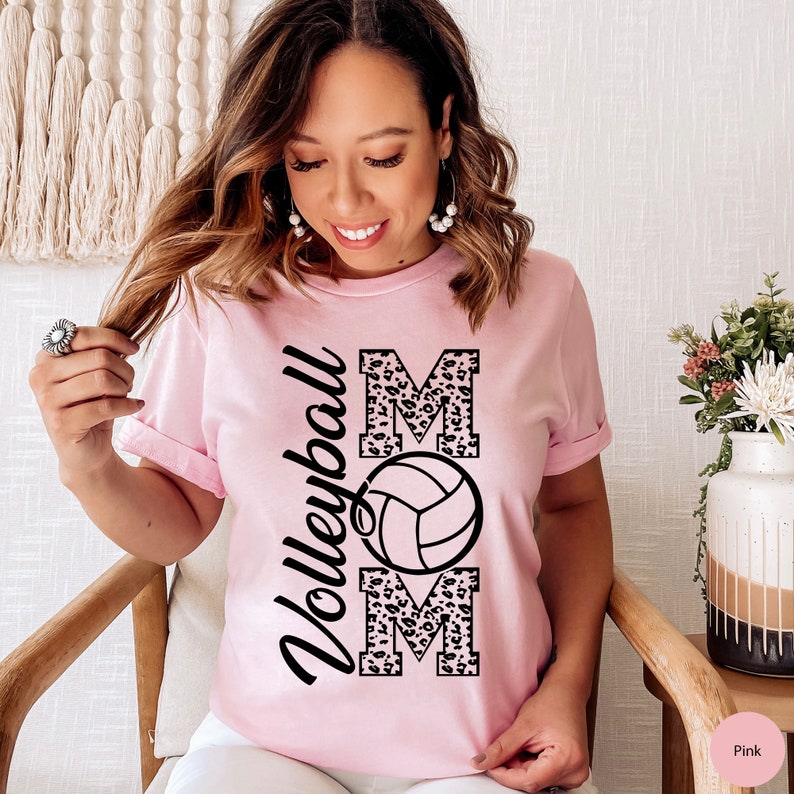 Peut inclure: T-shirt rose avec un motif l&eacute;opard noir et blanc qui dit "Volleyball Mom" avec un graphique de volley-ball au milieu.
