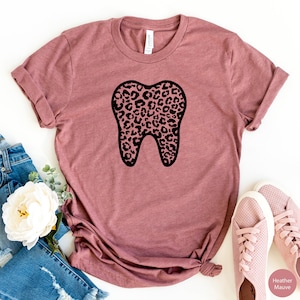May include: A heather mauve t-shirt with a black outline of a tooth. The tooth is filled with a leopard print pattern.