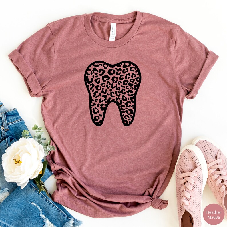 May include: A heather mauve t-shirt with a black outline of a tooth. The tooth is filled with a leopard print pattern.
