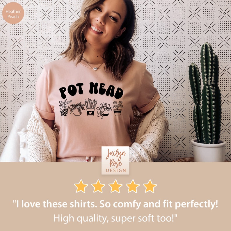May include: A pink t-shirt with the text "POT HEAD" in black lettering. The shirt features a graphic of five potted plants. The shirt is being modeled by a person. The text "Jaclyn Rose DESIGN" is visible below the graphic. Five stars are displayed below the text.