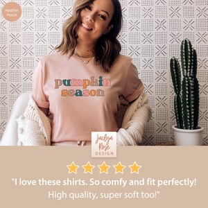 Puede incluir: Una camiseta rosa con el texto "pumpkin season" en letras de colores. La camiseta la lleva puesta una persona y tiene una calificaci&oacute;n de cinco estrellas con el texto "Me encantan estas camisetas. Son muy c&oacute;modas y me quedan perfectas. &iexcl;De alta calidad, s&uacute;per suaves tambi&eacute;n!"