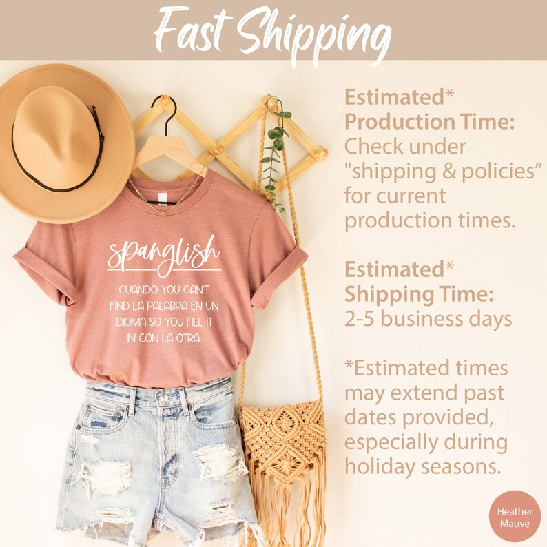 K&ouml;nnte beinhalten: Ein T-Shirt in Heather-Mauve mit dem Text "Spanglish" und dem Satz "CUANDO YOU CANT FIND LA PALABRA EN UN IDIOMA SO YOU FILL IT IN CON LA OTRA" in wei&szlig;er Schrift. Das Shirt h&auml;ngt an einem Holzb&uuml;gel mit einem Strohhut und einer geflochtenen Tasche.