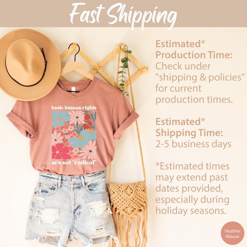 May include: A heather mauve t-shirt with a floral design and the text "basic human rights are not 'radical'" printed on the front. The shirt is displayed on a wooden hanger with a straw hat and a woven bag.
