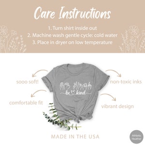 May include: Gray t-shirt with a white design that says "be kind" in sign language. The shirt is made in the USA and is made with non-toxic inks. The shirt is soft and comfortable.