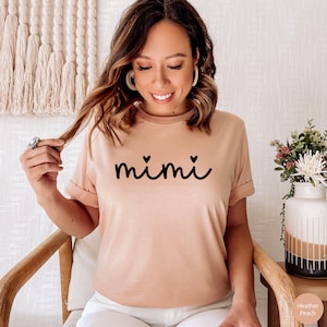 May include: A heather peach t-shirt with the word "mimi" in black script with two small hearts on either side of the word.
