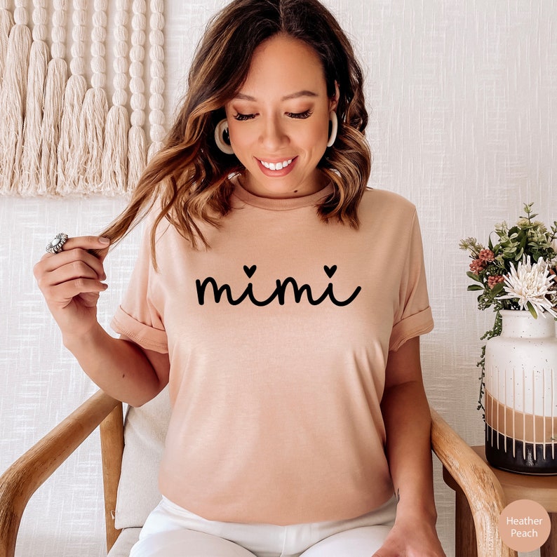 May include: A heather peach t-shirt with the word "mimi" in black script with two small hearts on either side of the word.