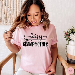 K&ouml;nnte beinhalten: Ein pinkfarbenes T-Shirt mit dem Text "fairy grandmother" in schwarzer Schrift. Der Text ist mit einem Stern und einer Linie &uuml;ber dem Wort "grandmother" gestaltet.