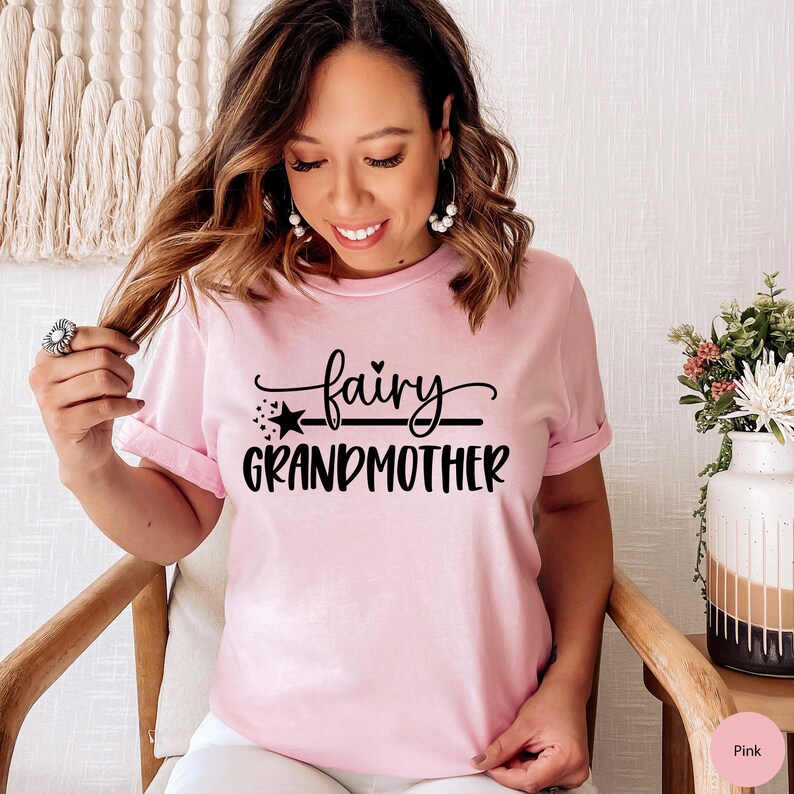 K&ouml;nnte beinhalten: Ein pinkfarbenes T-Shirt mit dem Text "fairy grandmother" in schwarzer Schrift. Der Text ist mit einem Stern und einer Linie &uuml;ber dem Wort "grandmother" gestaltet.