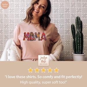 May include: A pink t-shirt with the word "MAMA" spelled out in colorful, decorative letters. The letters are decorated with floral patterns and a small image of the Virgin Mary. The shirt is being worn by a person with a smiling face. The text "Jaclyn Rose DESIGN" is visible below the shirt. Five stars are displayed below the text. The text "I love these shirts. So comfy and fit perfectly! High quality, super soft too!" is displayed below the stars.