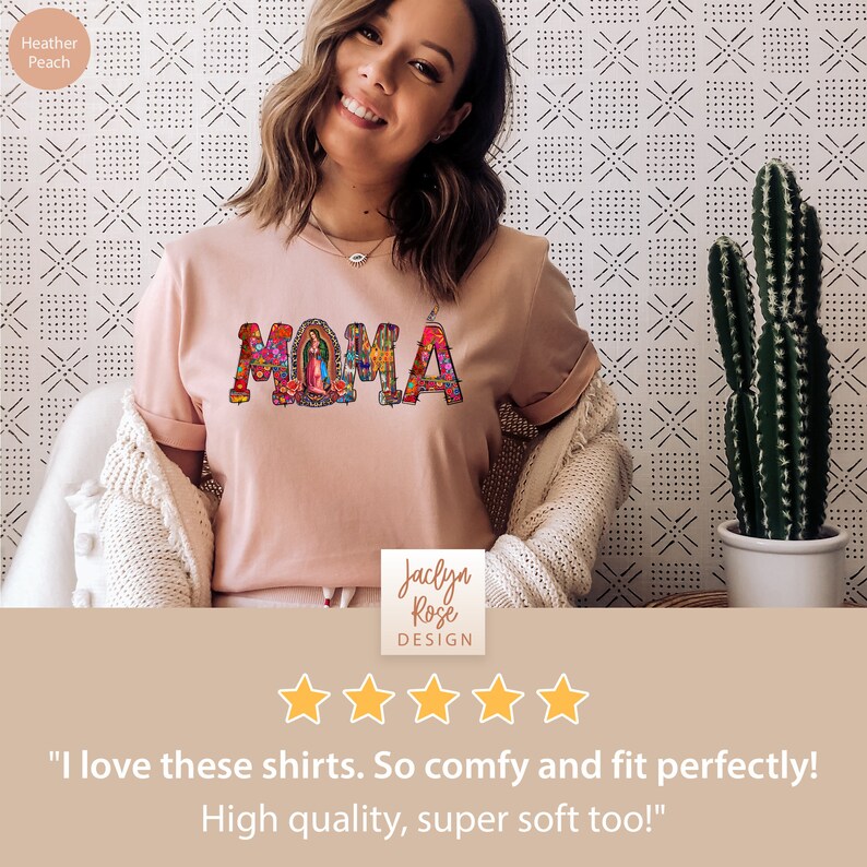 May include: A pink t-shirt with the word "MAMA" spelled out in colorful, decorative letters. The letters are decorated with floral patterns and a small image of the Virgin Mary. The shirt is being worn by a person with a smiling face. The text "Jaclyn Rose DESIGN" is visible below the shirt. Five stars are displayed below the text. The text "I love these shirts. So comfy and fit perfectly! High quality, super soft too!" is displayed below the stars.
