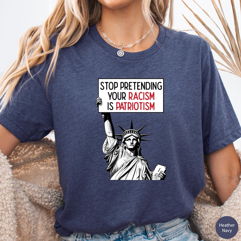 Peut inclure: Un t-shirt bleu marine avec un graphique de la Statue de la Libert&eacute; tenant une pancarte qui dit "Stop Pretending Your Racism Is Patriotism".