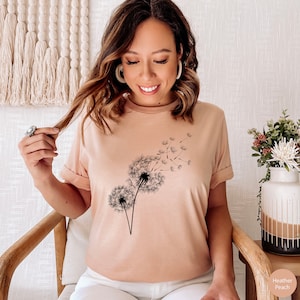 May include: A heather peach colored t-shirt with a black dandelion graphic. The dandelion has seeds blowing in the wind.