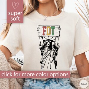 May include: A white t-shirt with a black and white illustration of the Statue of Liberty holding a sign that says "FDT". The sign is red, green, and yellow. The t-shirt is super soft.
