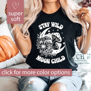 Puede incluir: Camiseta negra con texto blanco que dice "Stay Wild Moon Child". El dise&ntilde;o presenta una luna creciente con hongos y flores.