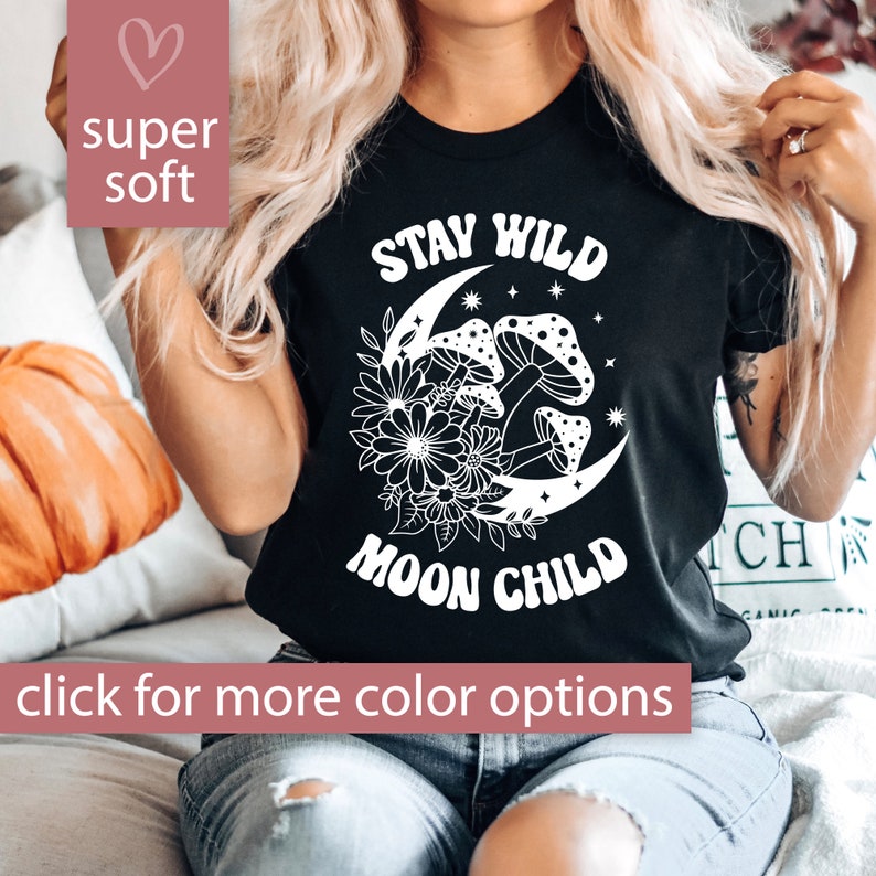 Puede incluir: Camiseta negra con texto blanco que dice "Stay Wild Moon Child". El dise&ntilde;o presenta una luna creciente con hongos y flores.