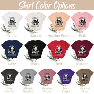 May include: A graphic t-shirt design featuring a skeleton holding a coffee cup with the text "Fueled by True Crime & Coffee". The shirt is available in 12 different colors: white, natural, heather peach, pink, navy, black, red, maroon, grey heather, athletic heather, heather mauve, team purple, and heather olive.