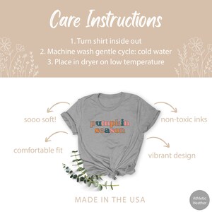 Puede incluir: Una camiseta gris con el texto "pumpkin season" en letras de colores. La camiseta est&aacute; hecha en los EE. UU. y presenta un ajuste c&oacute;modo, tintas no t&oacute;xicas y un dise&ntilde;o vibrante.