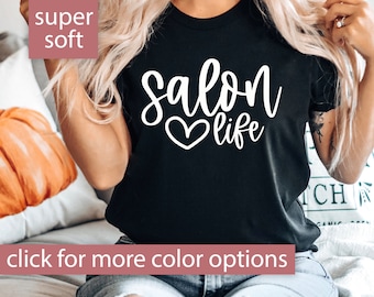 May include: A black t-shirt with the text "salon life" in white lettering with a heart symbol. The text is in a cursive font. The t-shirt is being worn by a person with long blonde hair.