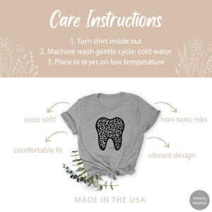 May include: A gray t-shirt with a black leopard print tooth graphic. The shirt is made of a soft, comfortable material and features a vibrant design. The text "sooo soft!" and "comfortable fit" are written on the left side of the image. The text "non-toxic inks" and "vibrant design" are written on the right side of the image. The text "Care Instructions" is written at the top of the image. The text "Made in the USA" is written at the bottom of the image. The text "Athletic Heather" is written in the bottom right corner of the image.