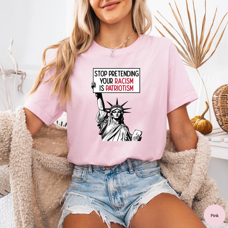 Peut inclure: Un t-shirt rose avec un graphique de la Statue de la Libert&eacute; tenant une pancarte qui dit "Arr&ecirc;tez de pr&eacute;tendre que votre racisme est du patriotisme".