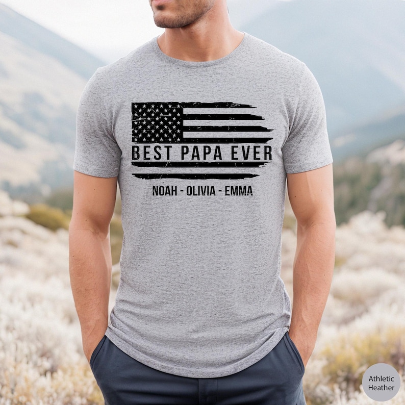 May include: A gray t-shirt with a distressed American flag design and the text "Best Papa Ever" with the names "Noah - Olivia - Emma" underneath.