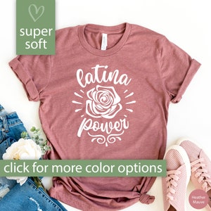 May include: A heather mauve t-shirt with the text "latina power" in white, featuring a white rose graphic. The shirt is displayed on a white background with jeans and shoes.