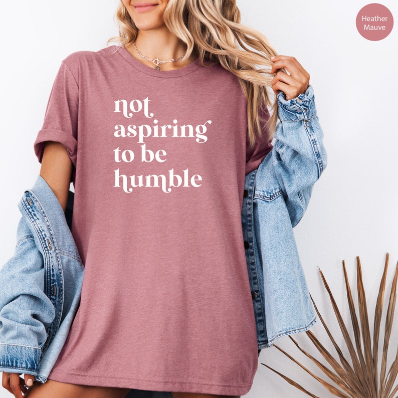 May include: A heather mauve t-shirt with the text "not aspiring to be humble" printed in white.