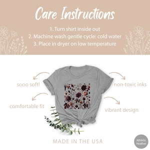 Op de afbeelding: Een heidegrijs T-shirt met een bloemenprint. Het shirt is gemaakt van zacht, comfortabel materiaal en is bedrukt met niet-giftige inkt. De tekst "sooo soft!" en "comfortable fit" staat aan de linkerkant van de afbeelding. De tekst "non-toxic inks" en "vibrant design" staat aan de rechterkant van de afbeelding. De tekst "MADE IN THE USA" staat onderaan de afbeelding. De tekst "Athletic Heather" staat in de rechterbenedenhoek van de afbeelding.