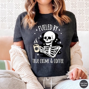 May include: Dark grey heather t-shirt with a skeleton holding a coffee mug and the text "Fueled by True Crime & Coffee".