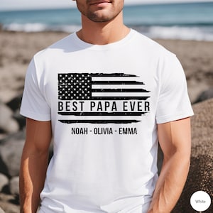 May include: White t-shirt with a distressed American flag design and the text "Best Papa Ever" with the names "Noah - Olivia - Emma" underneath.