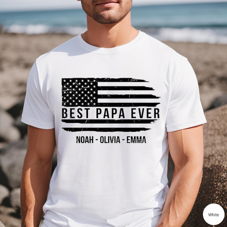 May include: White t-shirt with a distressed American flag design and the text "Best Papa Ever" with the names "Noah - Olivia - Emma" underneath.
