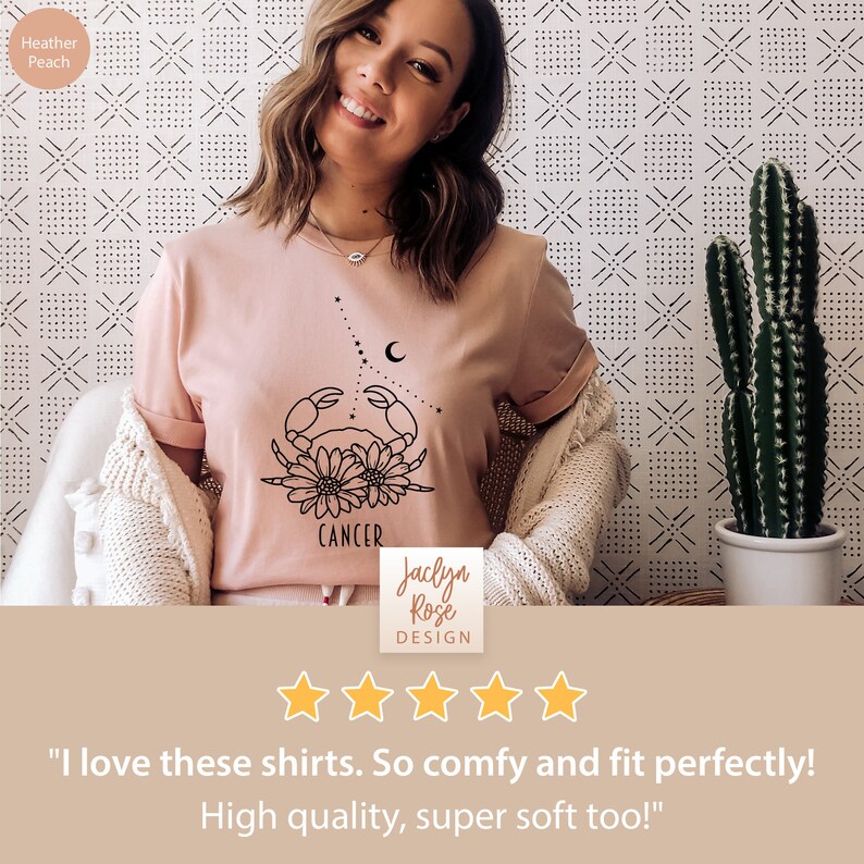 May include: A pink t-shirt with a black outline of a crab and flowers, with the word "Cancer" printed below. The shirt is worn by a person with a smiling face. The text "Jaclyn Rose DESIGN" is printed below the image. Five gold stars are displayed below the text. The text "I love these shirts. So comfy and fit perfectly! High quality, super soft too!" is printed below the stars.