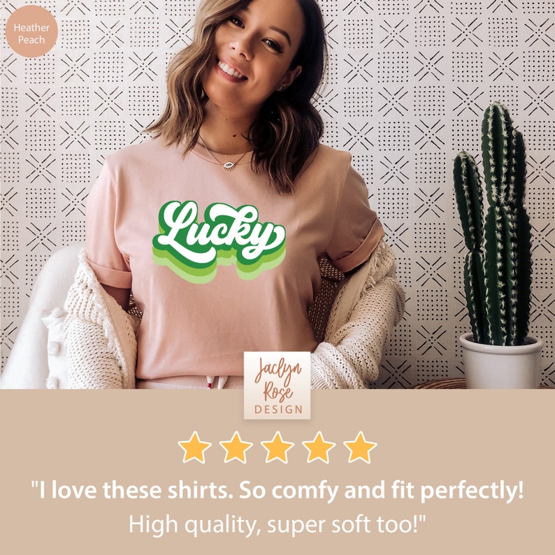 May include: A woman wearing a pink t-shirt with a green "Lucky" graphic. The shirt is a soft, comfortable material. The t-shirt is on a white background with a cactus in the background. The text "Jaclyn Rose DESIGN" is on the bottom of the image. The image has a five-star rating and the text "I love these shirts. So comfy and fit perfectly! High quality, super soft too!"