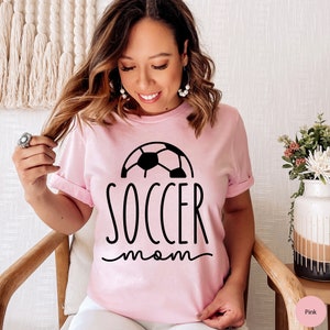 May include: Pink t-shirt with a black soccer ball graphic and the text "soccer mom" in black.